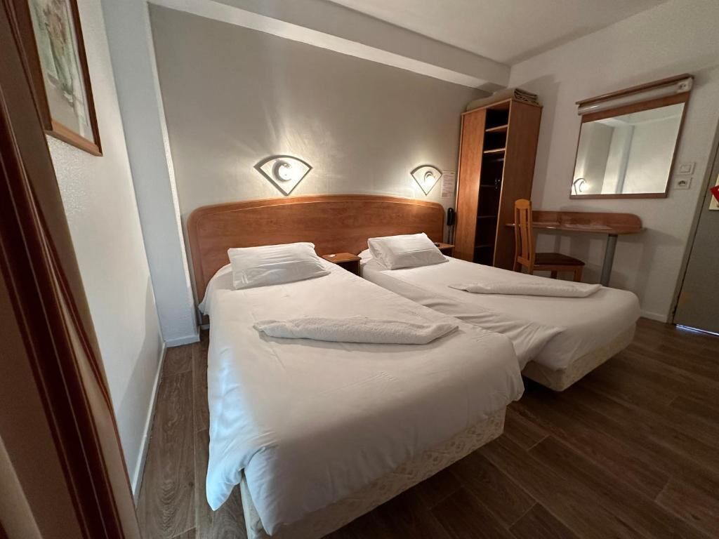 Habitación doble con dos camas, un armario de madera, un espejo y un escritorio pequeño.