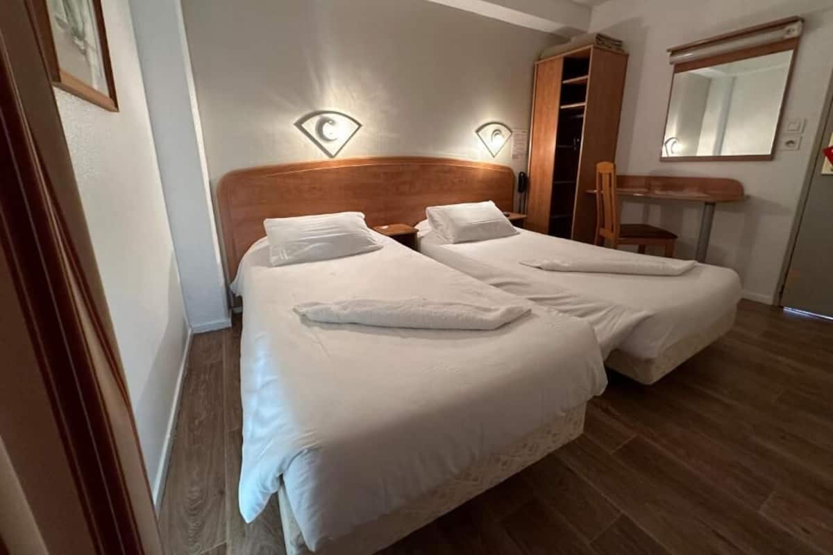 Une chambre double avec deux lits, une armoire en bois, un miroir et un petit bureau.
