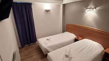 Una habitación de hotel con dos camas individuales, piso de madera, cortina azul y un aplique en la pared.