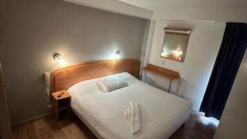 A hotel room with a wooden bed, bedside tables, a nightstand, and a mirror on the wall.