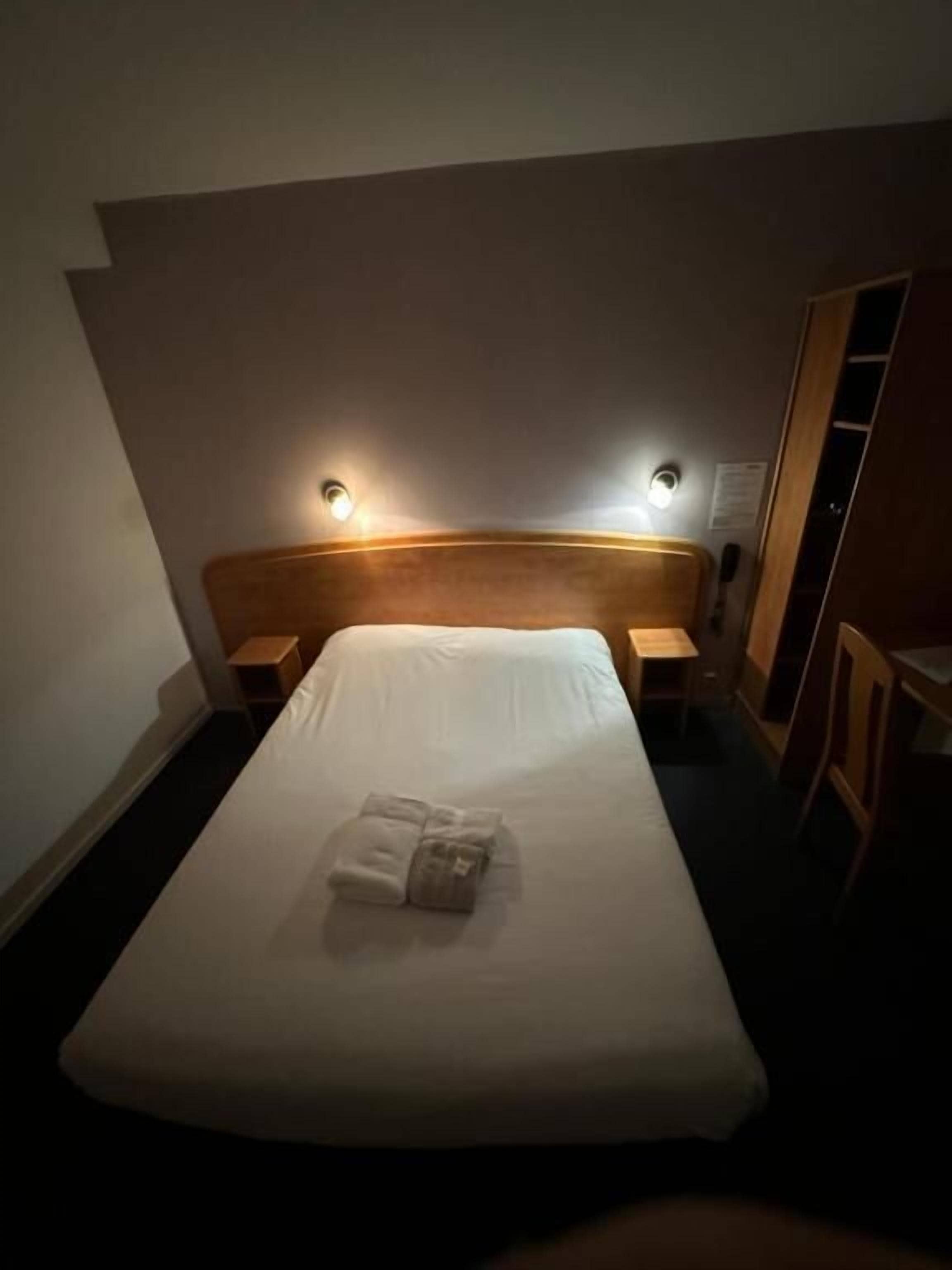 Ein Hotelzimmer mit einem Bett, zwei Nachttischen, einem hölzernen Kopfteil und Wandleuchten.