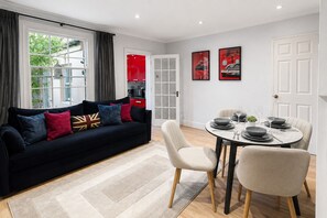 En moderne stue med en sort sofa, et spisebord dækket til fire personer, og et køkken i baggrunden.