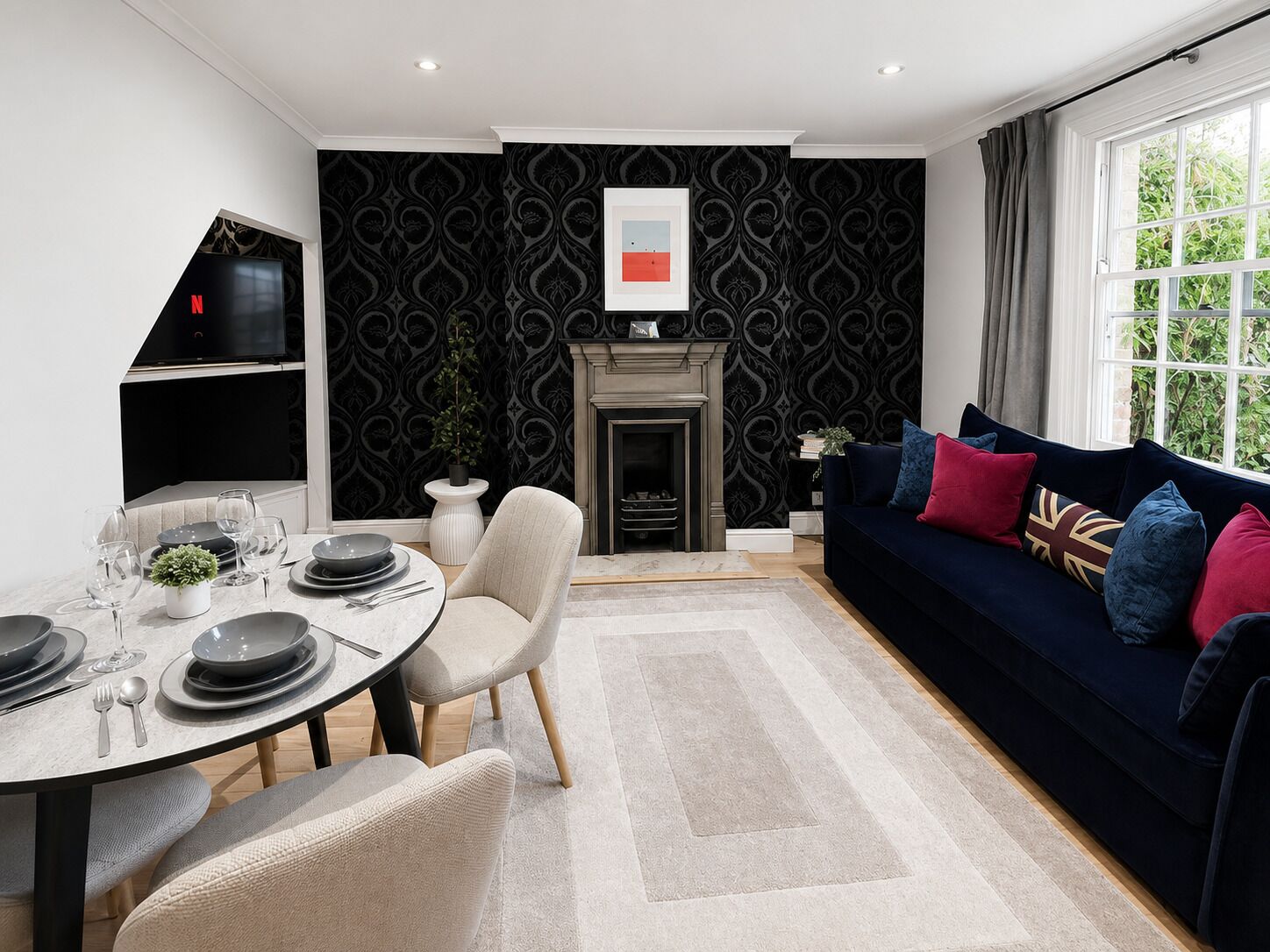 A modern living room with a fireplace, a dining area with a round table, and a sofa with colorful cushions.