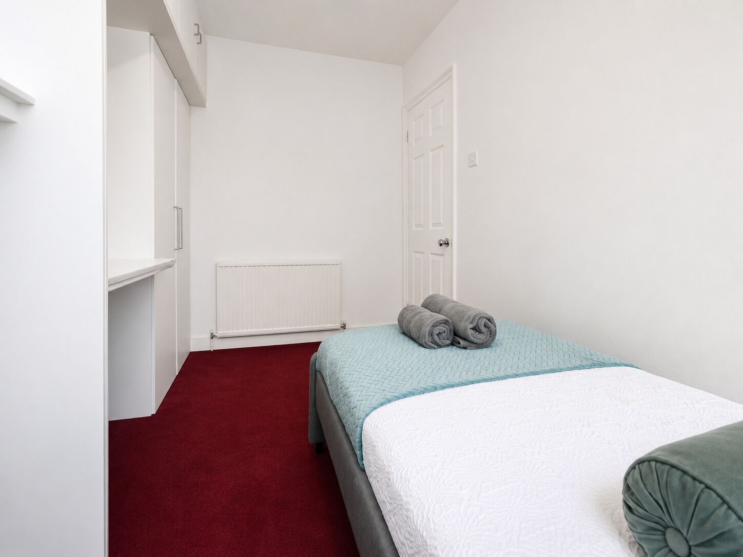 Ein Schlafzimmer mit einem Bett, einem Heizkörper, einer Tür und einem roten Teppich.