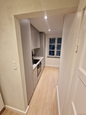 Eine schmale Küche mit Fenster, weißen Schränken und einem hellen Boden.