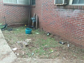 A backyard with a brick wall, a blue bucket, and scattered debris. - Marvelous 3-bedroom house with AC in charming Lanett (Lanett)