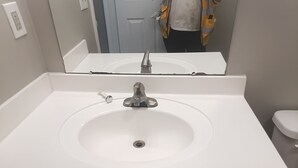 Un bagno con un lavandino bianco, uno specchio sopra e un water a destra.