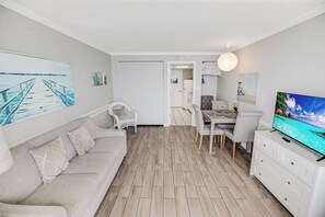 A modern living room with a sofa, dining table, and TV. - Oceanfront Condo - Sleeps 6 - Myrtle Beach (Myrtle Beach)