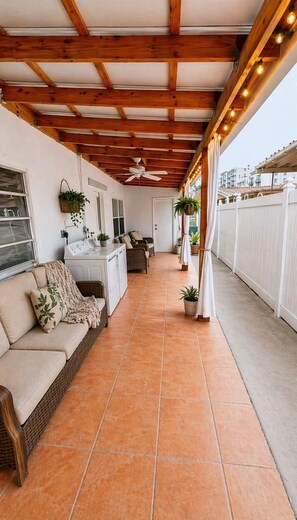 Ein überdachter Patio-Bereich mit einer Couch, einer Waschmaschine und einem Deckenventilator.