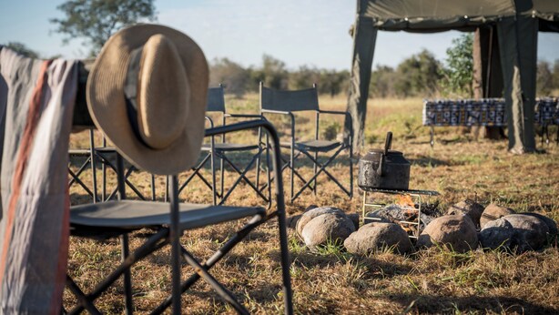 A campsite with a tent, a hat, a chair, and a portable stove. - Satara Wild Camp- Greater Kruger (Mpumalanga)