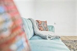 A light blue sofa with a knitted throw blanket and a patterned pillow against a white wall. - Cozy 1BR In Central Dallas Location Near FIFA WC (Dallas)