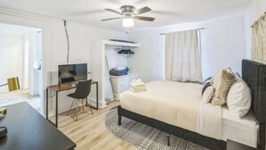 Ein Schlafzimmer mit einem Bett, einem Schreibtisch, einem Stuhl, einem Fernseher, einem Deckenventilator und einem Kleiderschrank.