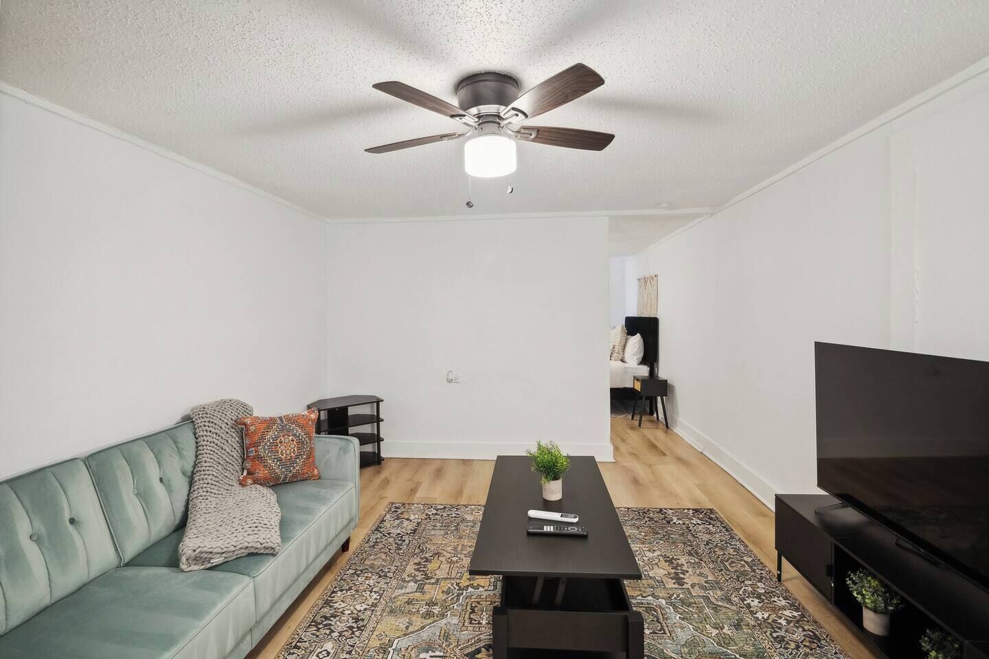 Ein stilvolles Wohnzimmer mit Sofa, Couchtisch, Fernseher und Deckenventilator.