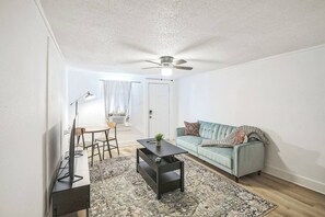 A compact living space with a ceiling fan, a sofa, a coffee table, a dining table with chairs, and a patterned rug. - Cozy 1BR In Central Dallas Location Near FIFA WC (Dallas)