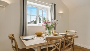 Ein Essbereich mit einem Tisch für vier Personen, einem Blumenstrauß und einem Fenster mit Vorhängen.
