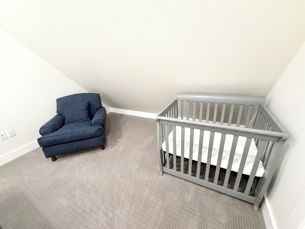 Una habitación con un sillón azul y una cuna gris.