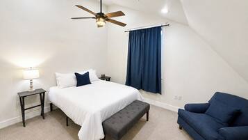 A bedroom with a bed, a bench, a chair, a lamp, a ceiling fan, and a window with curtains.