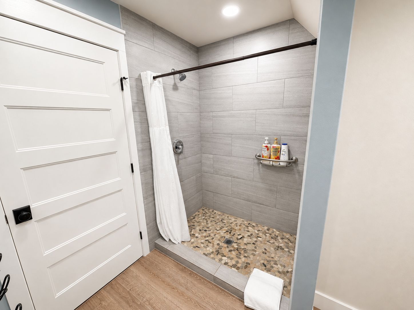 Une salle de bain moderne avec une douche, des murs carrelés, un plancher en bois et un porte-serviettes avec des articles de toilette.
