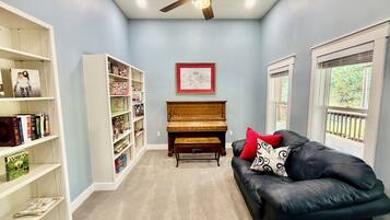 Una habitación con ventilador de techo, un piano, una estantería y un sofá de cuero.