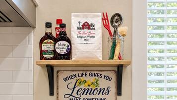 A kitchen with two waffle irons on a timer, bottles of syrup, a bag of waffle mix, and a sign with a lemon quote.