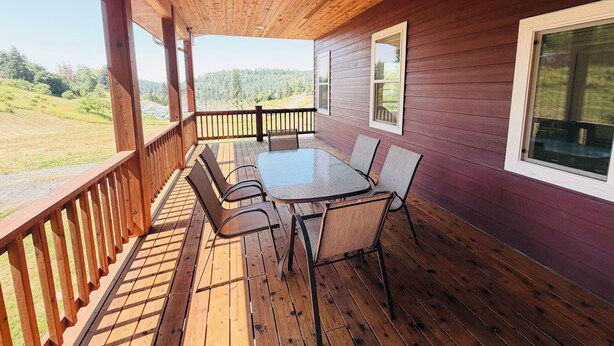 Une terrasse extérieure couverte, dotée d’une table et de chaises, de rampes en bois et offrant une vue sur un paysage verdoyant.