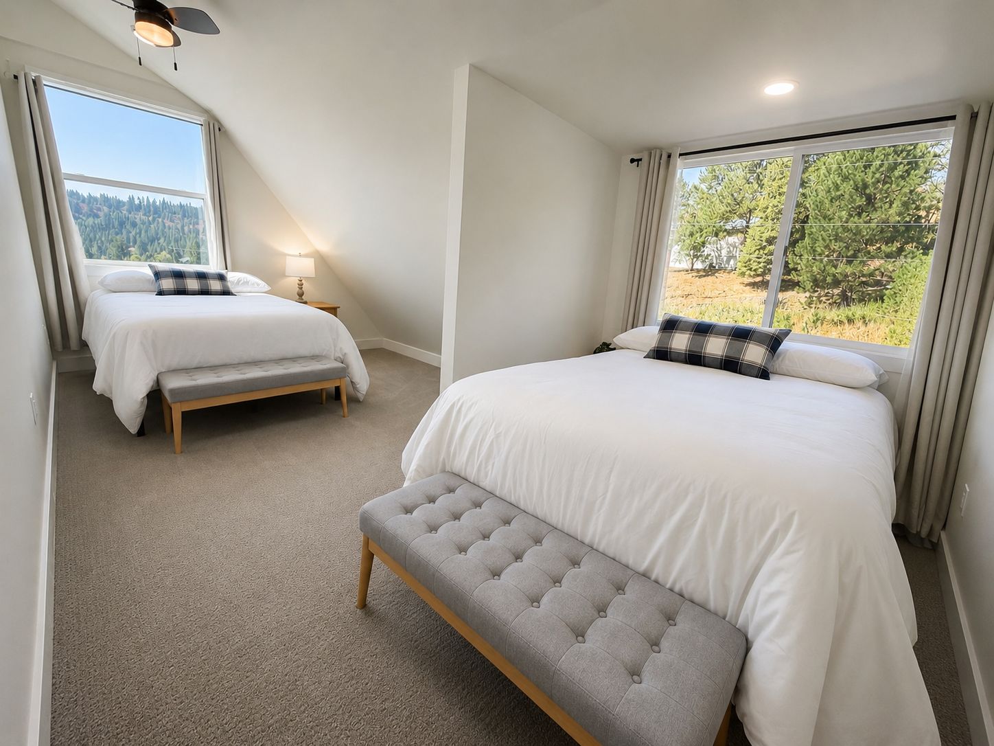 A bedroom with two beds, a bench, and a large window with a view of trees.