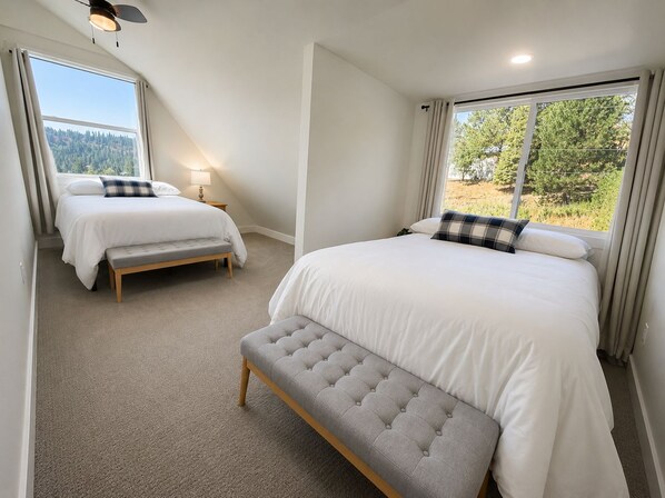 A bedroom with two beds, a bench, and a large window with a view of trees.
