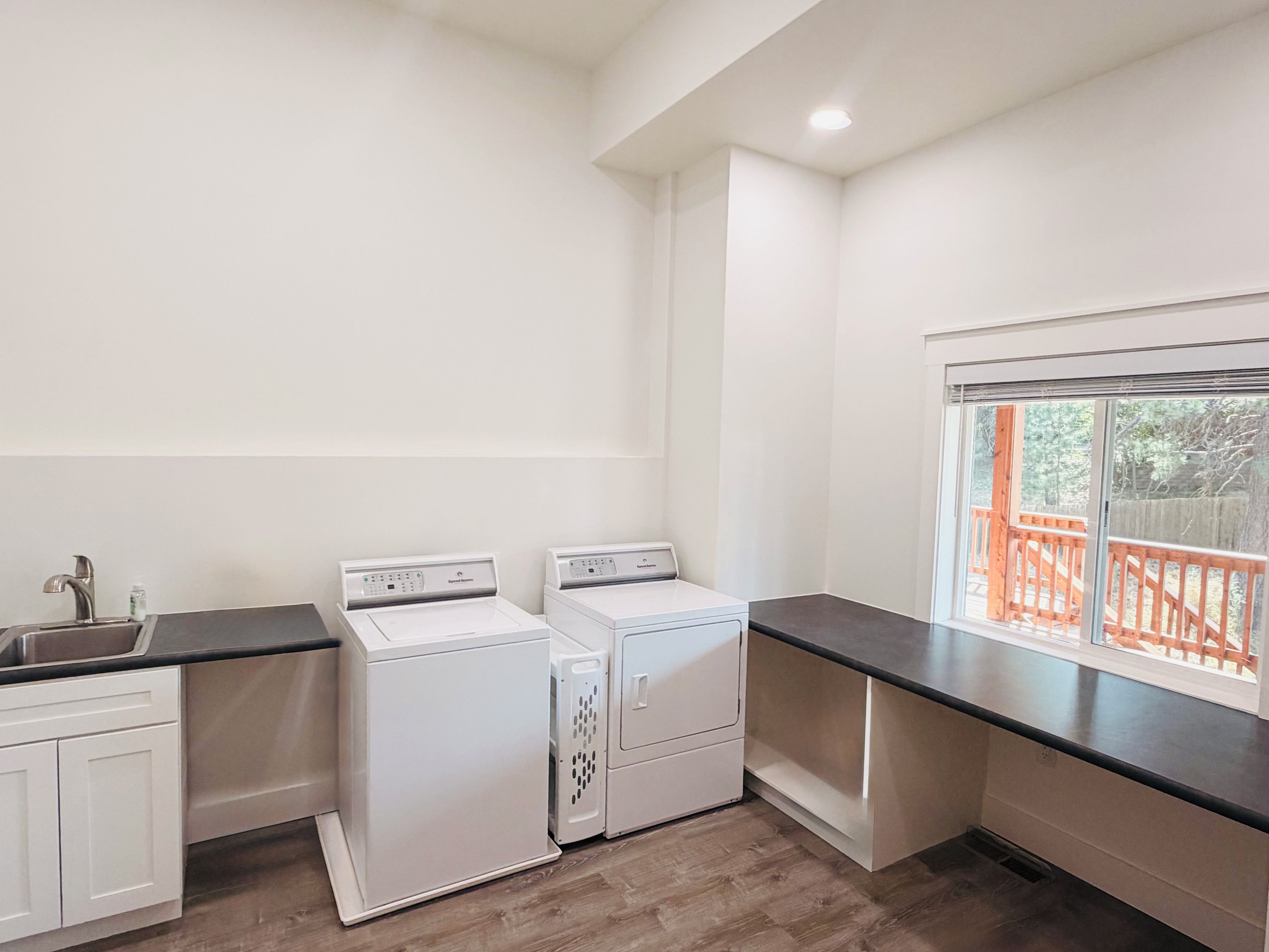 A laundry area with two washing machines, a sink, and a window with a view of a wooden deck.