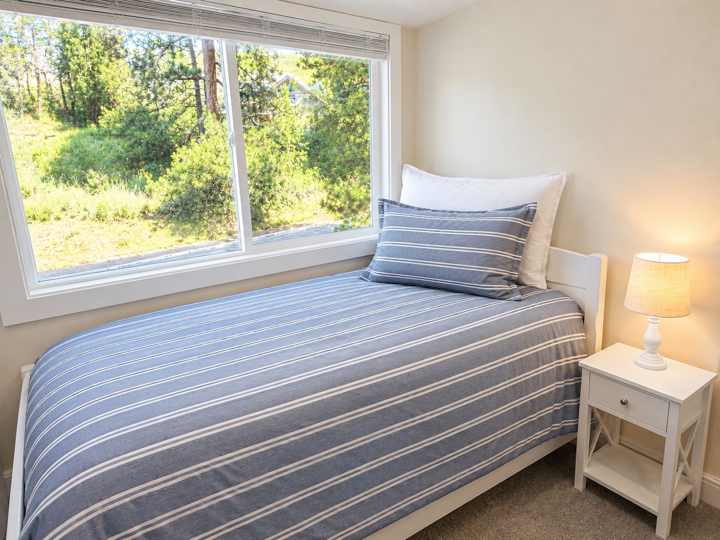 Un dormitorio con cama, mesita de noche, lámpara y ventana con vista a la vegetación.