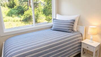 Un dormitorio con cama, mesita de noche, lámpara y ventana con vista a la vegetación.