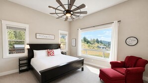 Une chambre à coucher avec un lit, un fauteuil rouge, un ventilateur de plafond et une grande fenêtre donnant sur un beau paysage.
