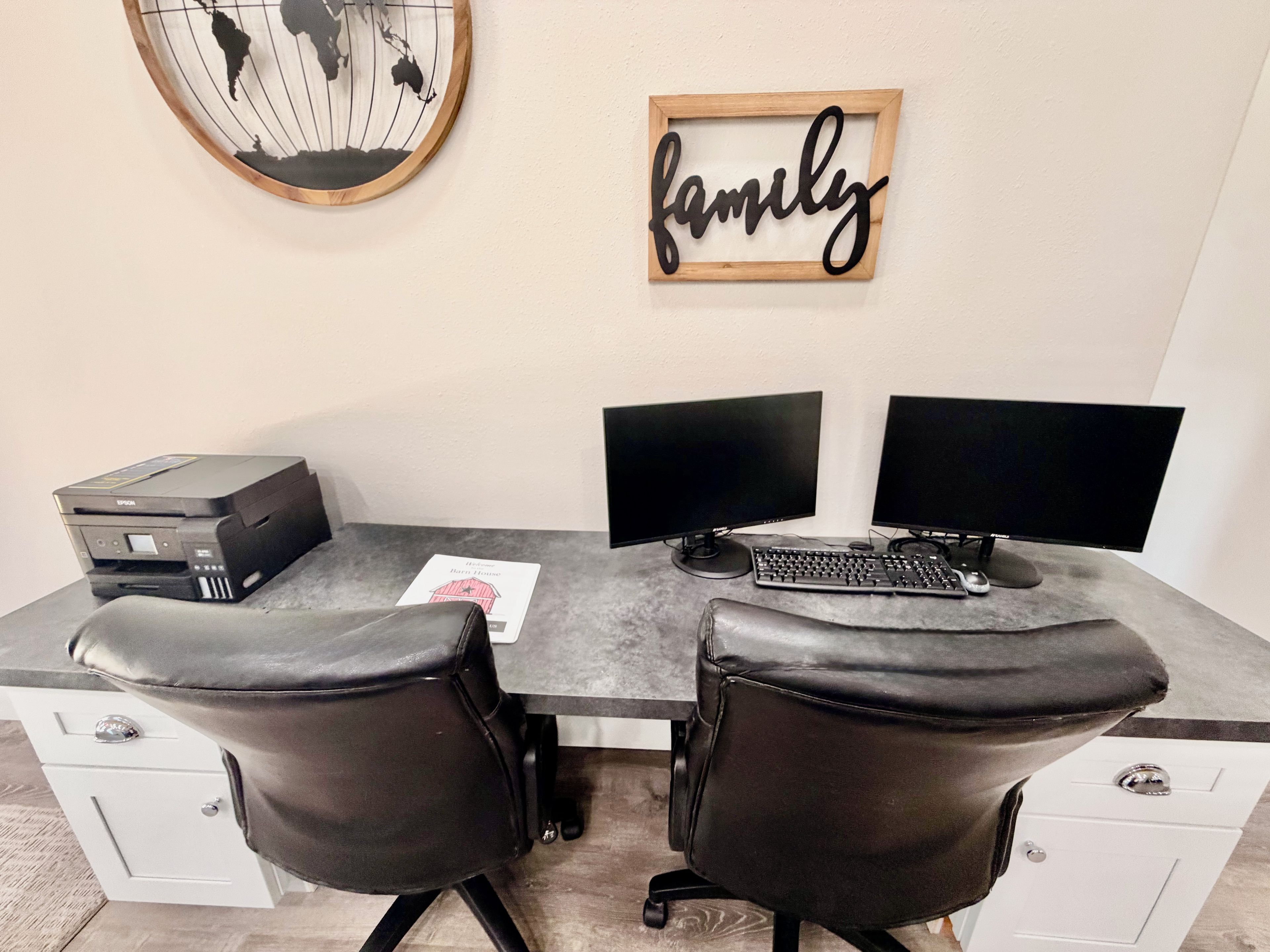 A home office setup with two monitors, a printer, and leather chairs.