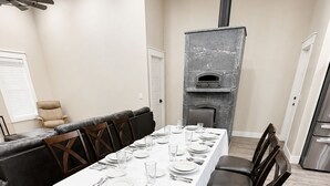 Un espace repas avec une longue table dressée pour six personnes, entourée de chaises, d’un canapé et d’une cheminée.