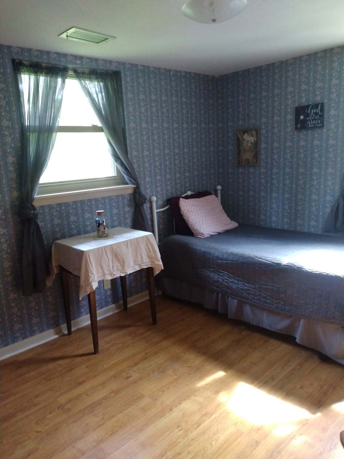 A bedroom with a single bed, a small table, and a window with curtains.