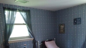 Quarto com uma cama de solteiro, uma mesinha e uma janela com cortinas.