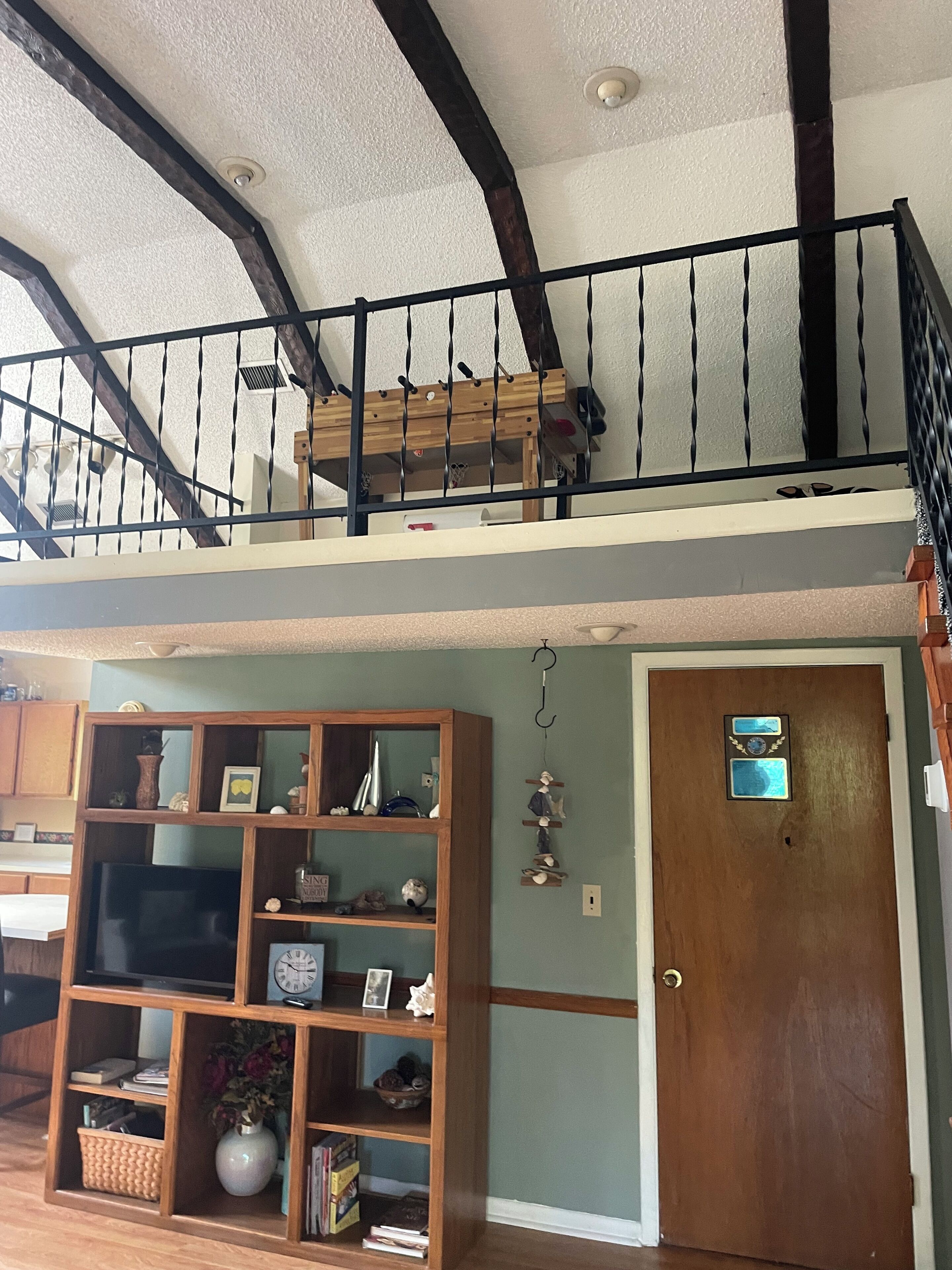 Um espaço de estar em vários níveis, com escada de madeira, estante e porta com detalhe decorativo.