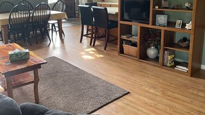Ampla sala de estar com pé direito alto, piso de madeira, mesa de jantar com cadeiras, sofá, estante e escada.