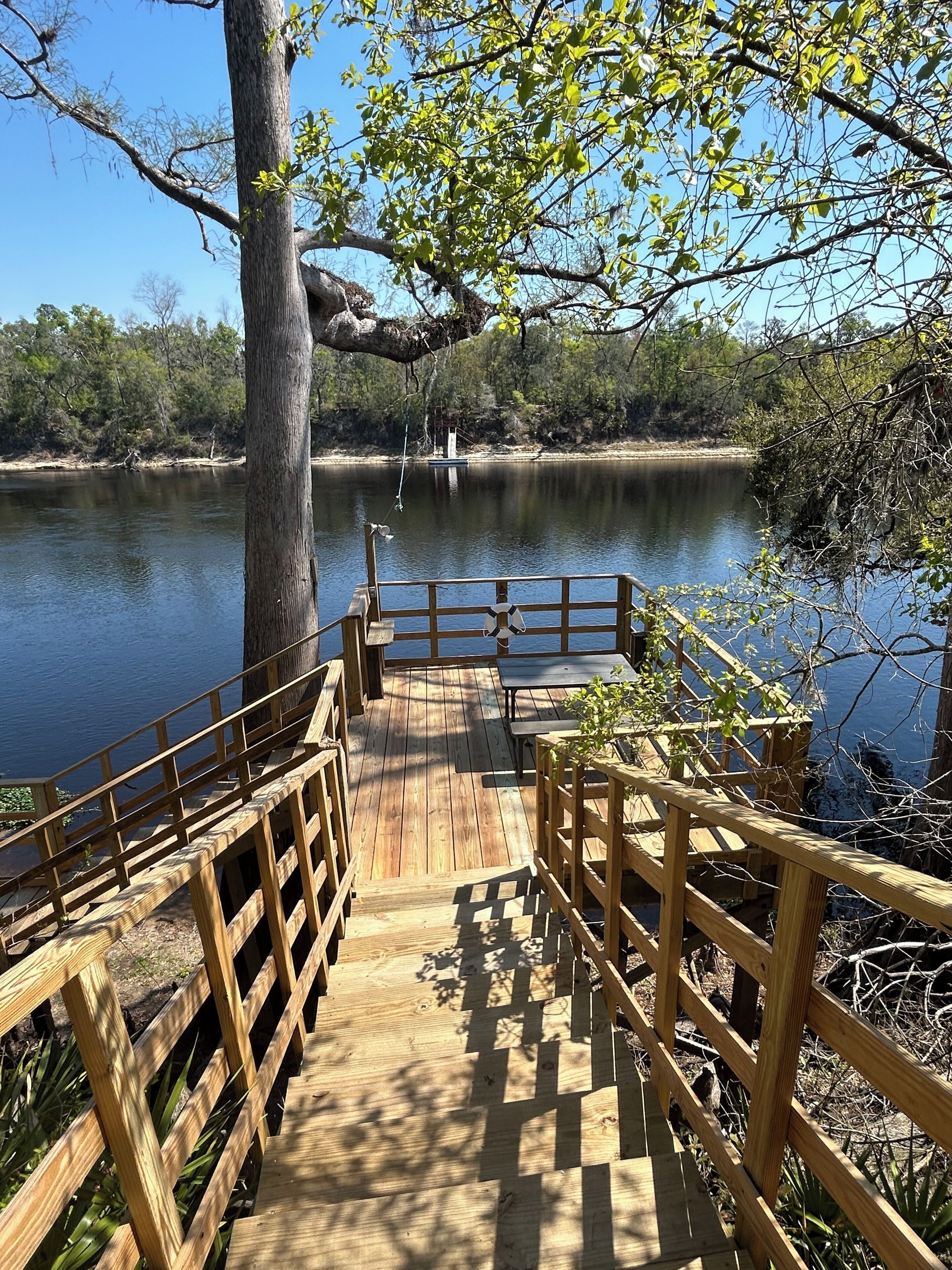 Une terrasse en bois qui mène à un lac, avec un banc et une bouée de sauvetage.