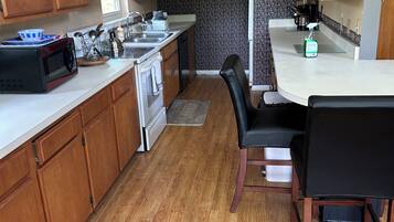 Cozinha compacta com armários de madeira, micro-ondas, fogão e área de jantar com mesa e cadeiras.