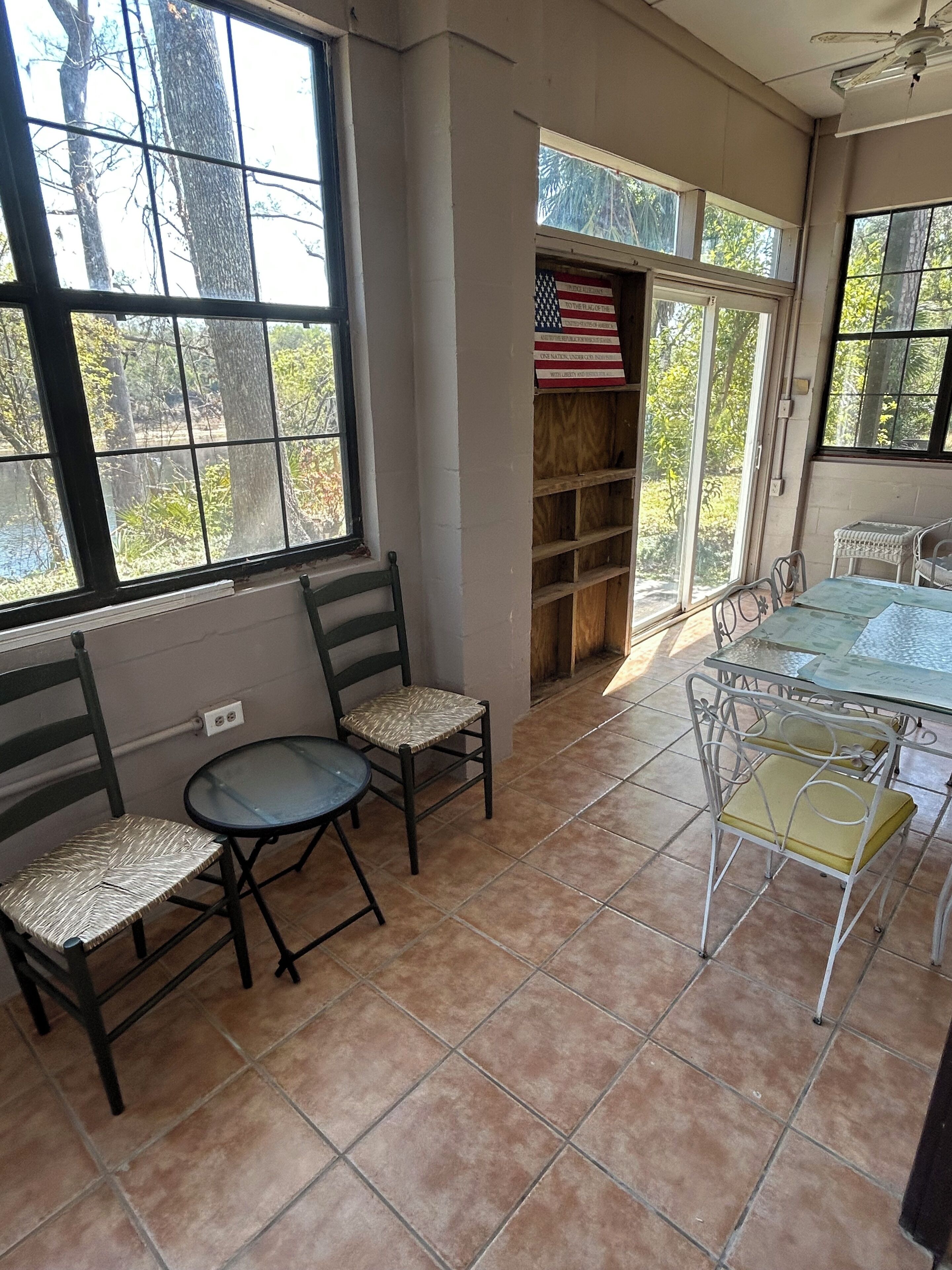 Una habitación luminosa con suelo de baldosas, una mesa con sillas y una ventana con vistas a árboles.