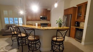 A kitchen with a central island, bar stools, a refrigerator, and wooden cabinets. - 3-bedroom + Den/2 Bath/2 Car Garage (Naples)