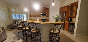 A kitchen with a central island, bar stools, a refrigerator, and wooden cabinets. - 3-bedroom + Den/2 Bath/2 Car Garage (Naples)