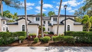 A multi-story residential building with a symmetrical facade, large windows, and a well-maintained garden with palm trees and shrubs. - 3-bedroom + Den/2 Bath/2 Car Garage (Naples)