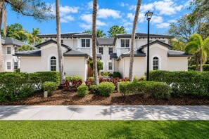 A multi-story residential building with a symmetrical facade, large windows, and a well-maintained garden with palm trees and shrubs. - 3-bedroom + Den/2 Bath/2 Car Garage (Naples)