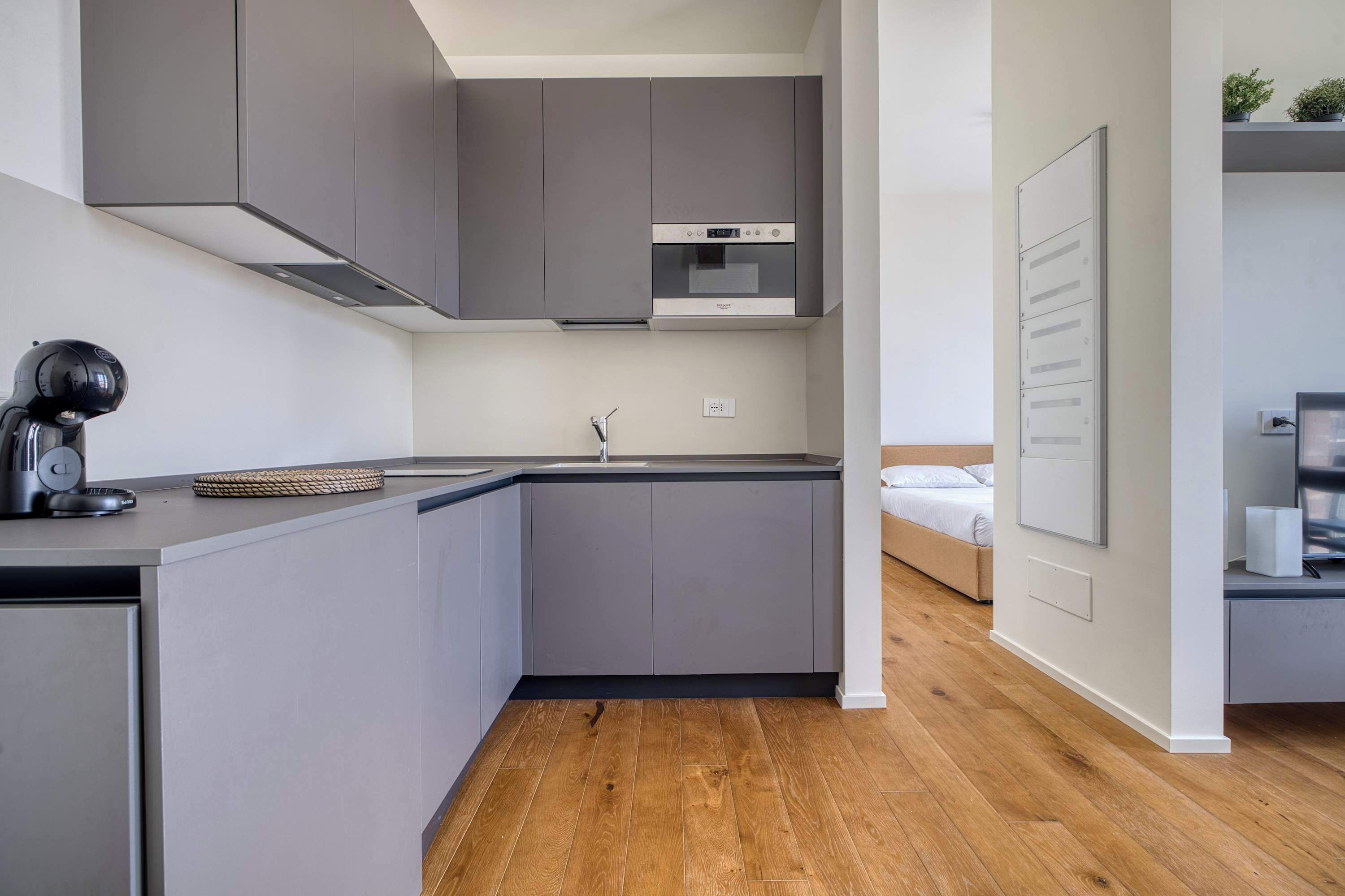A modern kitchen with grey cabinets, a built-in oven, and a wooden floor.