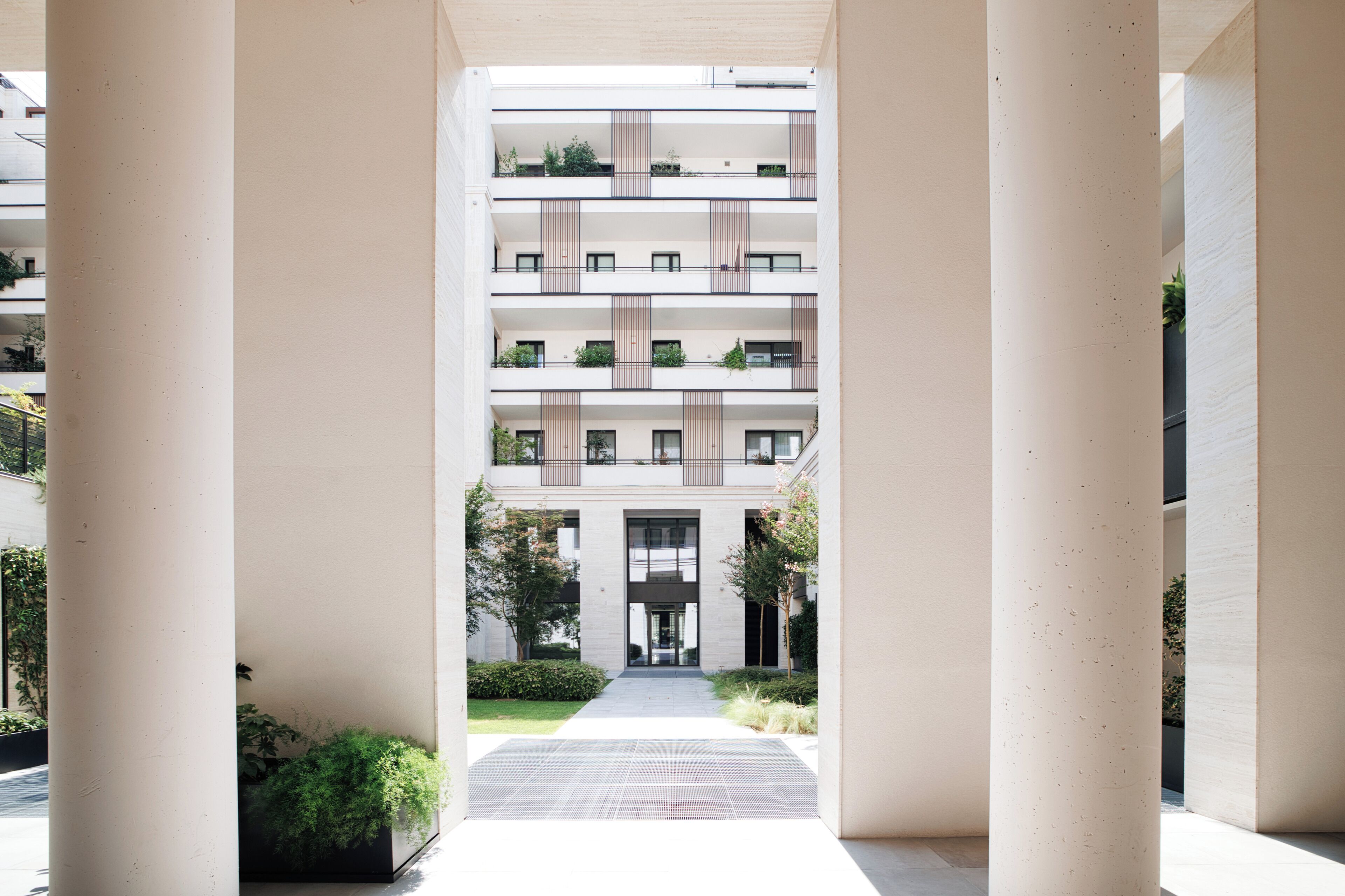 Un moderno edificio residencial de varios pisos con un patio central, balcones con vegetación y un diseño arquitectónico limpio.
