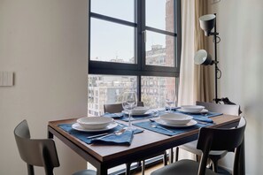 Taula de dinar preparada per a quatre amb plats, gots i coberts, situada davant d'una finestra gran amb vista a edificis.