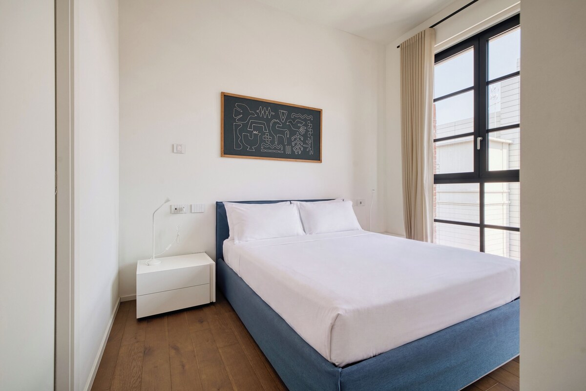 Une chambre à coucher avec un lit, une table de chevet et une œuvre d’art accrochée au mur.