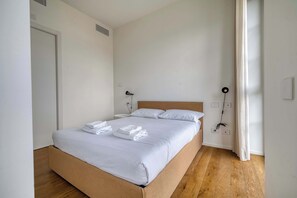 A neatly made bed with white linens, a wooden headboard, and a bedside table with a lamp. - Bright 1BR near to the center of Milan (Milano)