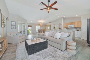 A spacious living room with a large sofa, a coffee table, and a ceiling fan. - Sunset Paradise! Heated pool, 3/2 plus office- Yes Dogs! Fenced, LUXE Upgrades! (Cape Coral)
